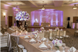 Indoor reception with long tables, purple flowers and purple uplighting
