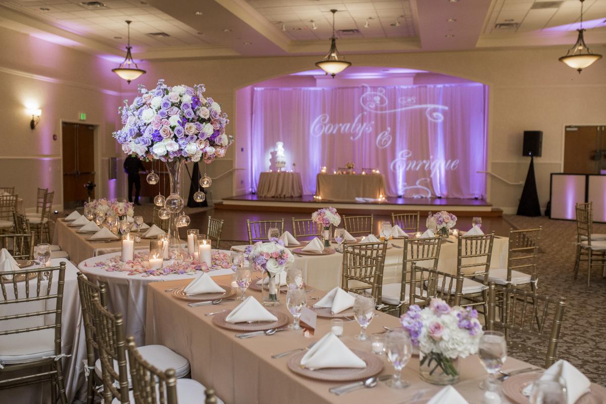 Indoor reception with long tables, purple flowers and purple uplighting